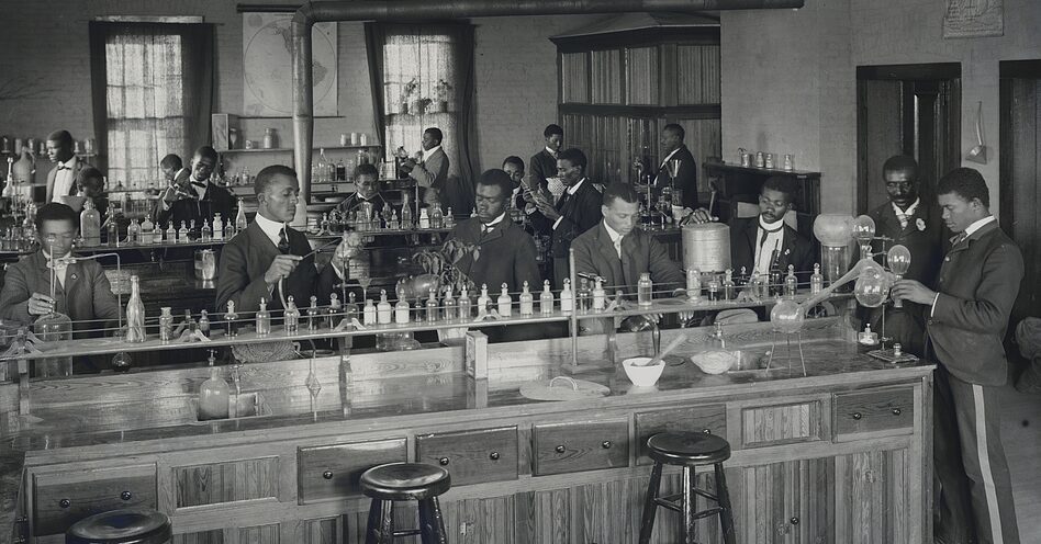 George Washington Carver (second from right) with students in the chemistry laboratory at Tuskegee Institute, ca. 1902.